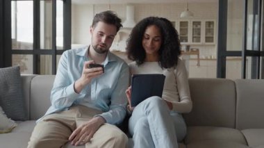 Neşeli Çift Rahatlatıcı Koltuk, Erkek Uzaktan Tutma, Tablet Ekranla Nişanlı Kadın. Konforlu Ev Ayarlama, Modern Yaşam Tarzı, Dijital Eğlence, Konforlu Atmosfer, Kaliteli Zaman, Gülümseme, Nişanlı