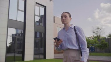 İş kadını modern ofis binasının yakınında yürürken acil mesajı kontrol ediyor. Resmi Giyimde Kendine Güvenen Kadın Profesyonel Çağdaş Cam Mimarisini Geçerken Akıllı Telefona Odaklandı
