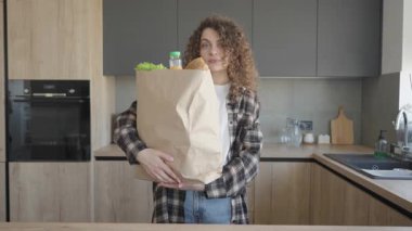 Mutfakta alışveriş poşeti tutan kadın. Kamera yavaşça uzaklaşıyor. Sağlıklı Yaşam, Ev Yaşamı, Organik Gıda, Yemek Hazırlama, Parlak Modern İç Kesimlerde Günlük Ev Sahneleri İçin Mükemmel Görsellik