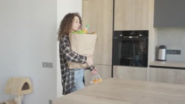 Kadın süpermarketten döndükten sonra mutfaktaki eşyaları boşaltıyor. Sağlıklı Yaşam Tarzını Gösteren Günlük Günlük rutin Anı, Taze Yemek Alışverişi, Samimi İç İşleri. Yüksek kalite 4k görüntü