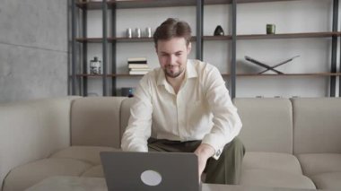 Modern iç mekanda bilgisayarla uzaktan kumandayla düşünen dalgın bir adam. Uzak çalışma, odaklanmış karar verme, yaratıcılık süreci kavramları için ideal bir görsel. Yüksek kalite 4k görüntü