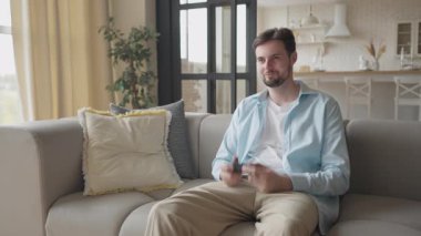 Genç adam evinde rahat bir koltukta otururken video oyunu hareketine daldı. Odaklanmış Bakış ile Oyun Oturumuna Girmek, Rastgele Atmosfer, Rahatlatıcı Haftasonu Sahnesi