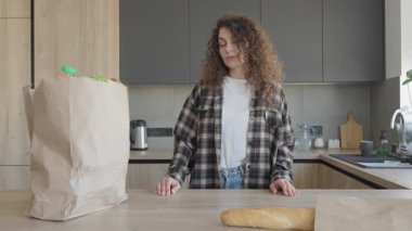 Bright Cozy Kitchen 'da alışveriş yaptıktan sonra çay yapan kadın. Günlük rutin anlar genç bir bayanın sıcak içeceğinin keyfini çıkardığı marketler ve doğal ışıklarla çevrili.