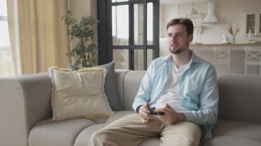 Modern Salonda Video Oyunu Zaferini Neşeli İfadeyle Kutlayan Adam. Dinamik Sahne Heyecan ve Duygusallık, Oyun oynamak ve ev ortamında eğlenmek için mükemmel