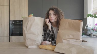 Alışveriş gezisinden sonra alışveriş poşetlerini açmadan önce kadın mutfakta dinleniyor. Genç bayan market koşusundan sonra duraklıyor, etrafı kağıt torbalarla çevrili, modern mutfak içinde. Günlük Rutin Temalar