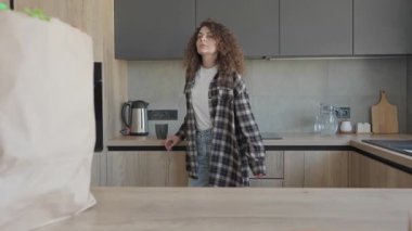 Alışveriş poşetlerini açtıktan sonra Modern Kitchen 'da Akıllı Telefon Kullanan Kadın. Stylish Kitchen 'ın iç kısımlarında rahat kadın arama telefonu, Üretici Market ziyaretinden sonra yeni alışverişlerle çevrili.