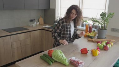 Kadın, alışveriş yaptıktan sonra mutfak tezgahında taze meyve ve sebze ayırıyor. Bakkaliyeyi tipe göre düzenlemek, parlak ev içi renkler. Sağlıklı Yaşam ve Gıda Organizasyonu Temaları İçin Mükemmel