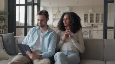 Koltukta oturan, tablet kullanan, ekranı gösteren, gülümseyen bir çift. Konforlu Ev Atmosferi, Paylaşılan Dijital Deneyim, Birlikte Tarama veya Planlama, Mutlu İlişki Anı