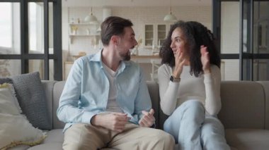 Çift kanepede birlikte gülüyor, şakacı bir şekilde işaret ediyor, eğlenceli sohbetin tadını çıkarıyor. Mutlu İlişkiler Anı Evde Doğal Işık, Samimi Duygular, Sıradan Kıyafetler, Evde Neşeli Bağlanma