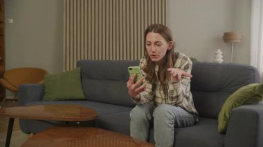 Videoda sohbet eden rahat genç bir kadın, koltukta hareketli bir şekilde. Otantik Uzaktan İletişim Anı, Evde Rahat, Sanal Konuşma sırasında Duyguları Özgürce İfade Etme