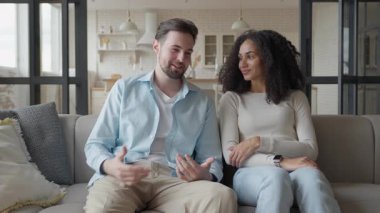 Kanepede oturup sohbet eden ve sıcak, modern oturma odasında içten bir gülümsemeyle gülümseyen çift. Rahat ve Şefkatli Etkileşim, Doğal Işık Atmosferi, Ev Konforu, Gerçek İlişki, Olumlu Duygular