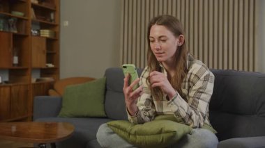 Samimi oturma odasındaki kanepede sohbet ederken duygusal kız hareketi. Etkileyici İletişim, Gelişigüzel Kıyafetler, Gevşek Vibe, Gerçek-zamanlı Bağlantı, Doğal Işık, Otantik İnsan Duygusu