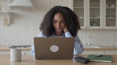 Mutfak masasında dizüstü bilgisayarda sakin bir ifadeyle yazan odaklanmış bir kadın. Parlak Mutfak İçi 'nde Konsantre Freelancer ya da Uzaktan İşçi Yakınındaki Kahve ile Barışçıl Çalışıyor