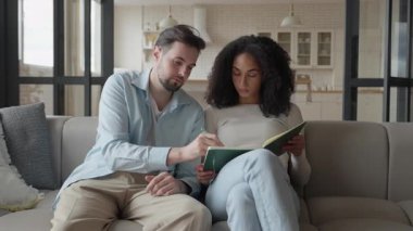 Kadın Beyin Fırtınası seansı sırasında not alırken Erkek Fikri Açıklıyor. Proje üzerinde çalışan yaratıcı çift, parlak modern oturma odasında koltukta oturmuş, odaklanmış ve meşgul ifadelerle...