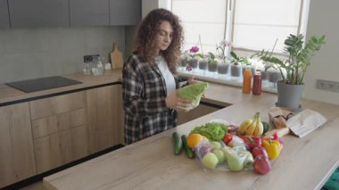 Gülümseyen Kadın Marul Tutuyor ve Sunlit Kitchen 'da Taze Market' e hayranlık duyuyor. Mutlu Kadın Sağlıklı Yaşam Tarzı, Organik Gıda Seçimleri, Parlak Doğal Işık, Modern Mutfak Atmosferi