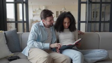 Çift evdeki koltukta aynı kitabı okumak için şakalaşıyor. Rahatlatıcı Etkileşim Sahası, İlişki Dinamikleri, Ortak İlgi Alanları ve Günlük Mizah gibi kavramlar için ideal