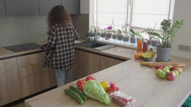 Yiyecek paketlerini açtıktan sonra tahta kesme tahtasını mutfak tezgahına koymak. Sunlit Modern İçi Taze Meyve ve Sebzelerle Sağlıklı Ev Yemeği Hazırlanıyor