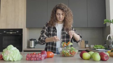 Kıvırcık saçlı kadın ev mutfağında taze sebze salatası servis ediyor. Sağlıklı Yeme Konsepti, Konforlu İçişleri, Organik Malzemeler, Günlük Yemek Düzenleme, Doğal Gıda Hazırlama