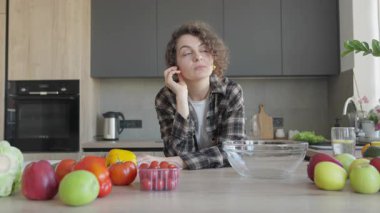 Parlak ev mutfağındaki masadaki malzemelere dikkatlice bakan bir kadın. Yaratıcı Yemek pişirme havası, Doğal Işık, Sağlıklı Yaşam Tarzı Konsepti, Taze Sebzeler, Günlük İçişleri, Barışçıl Günlük Günlük Rutin