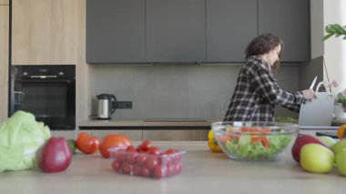 Kadın, salata yaptıktan sonra kesme tahtası, parlak mutfakta sohbet. Günlük Mutfak Rutini, Ev Atmosferi, Doğal Işık, Gerçek Yaşam Anı, Sağlıklı Yaşam Tarzı, Günlük Konuşma, Taze Malzemeler