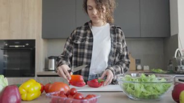 Mutfak tezgahında kırmızı biber dilimleyen kadın taze sebzelerle çevrili. Sağlıklı Aşçılık Süreci, Doğal Malzemeler, Ev Mutfağı Sahnesi, Organik Gıda, Parlak Işık, Günlük Yaşam Stili