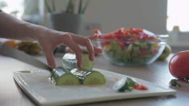 Yakından çekilen eller salatalığı taze salata kasesiyle doğruyor. Sağlıklı Yeme, Taze Malzemeler, Ev Yemeği, Vegan Yaşam Tarzı, Organik Yemek Hazırlama, Temiz Mutfak Sahnesi