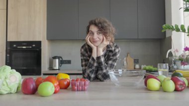 Kameraya gülümseyen bir kadın çerçeveyi genişleterek rengarenk mutfak sahnesini ortaya çıkarıyor. Parlak Doğal Işık, Taze Sebzeler Rahat Atmosfer, Pozitif Vibe, Ev Yaşam Tarzı, Gerçek An, Otantik Günlük Ayarlama