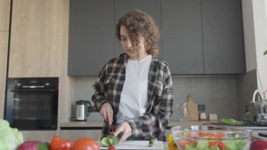 Kadın, taze ev yapımı salata hazırlarken mutfak tezgahında salatalık dilimliyor. Evde Sağlıklı Pişirme, Doğal Malzemeler, Parlak İçişleri, Organik Gıda, Gerçek Yaşam Anı, Basit Yaşam Tarzı