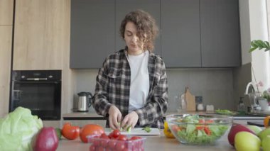 Parlak mutfağa taze sebze salatasıyla dilimlenmiş salatalığı kaseye ekliyorum. Sağlıklı Pişirme Süreci, Organik Malzemeler, Doğal Işıklı Ev Yapımı Yemekleri Hazırlama