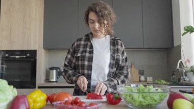 Mutfak masasında taze sebzelerle kırmızı biber doğrayan kadın. Sağlıklı Yemek Sahnesi, Organik Malzemeler, Günlük Yaşam Tarzı, Doğal Işık, Ev Atmosferi, Gıda Hazırlama