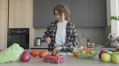 Mutfakta taze malzemelerle çevrili sebzeleri doğramaya odaklanmış bir kadın. Ev Pişirme Süreci, Sağlıklı Yaşam Tarzı, Gerçek Gıda Hazırlama, Organik Yemek Fikirleri, Parlak İçişleri, Gün Işığı Ambiansı