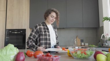 Bright Kitchen 'da salatayı hazırladıktan sonra tahtayı kırıntılarla kesen kadın. Yemek pişirme sürecinin sonu, günlük ev sahnesi, sağlıklı yaşam tarzı, taze malzemeler, gerçek an, temizlik rutini.