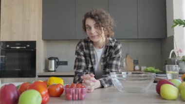 Mutfakta sebzelerle, günlük ruh haliyle, sağlıklı yaşam tarzıyla, organik yemek düzeniyle, sakin bir ifadeyle, ev içi, otantik günlük anlarıyla kameraya bakan düşünceli bir kadın.