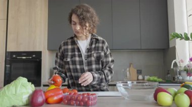 Parlak mutfakta domates toplayan ve sebzeleri inceleyen bir kadın. Sağlıklı Gıda Seçimi, Sabah Rutini, Organik Yaşam tarzı, Doğal Işık, Taze İçindekiler, Gerçek Hayat Anı