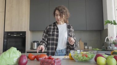Domates tutan ve ev mutfağında bir sonraki aşamayı düşünen bir kadın. Sağlıklı Yemek Hazırlama Anı, Taze Malzemeler, Mutfak Süreci, Samimi İçişleri, Gerçek Hayat Sahnesi, Yavaş Yaşayan Ruh Durumu