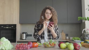 Mutfakta salatayla dikilirken telefonda kötü haber okuyan dehşete düşmüş bir kadın. Parlak Ev İçi 'nde Duygusal Tepki, Hayattaki Zorluklar, Şok ya da Hayal kırıklığı konulu Konular İçin İdeal