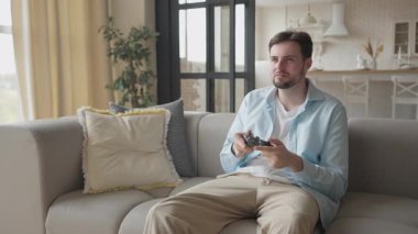 Oturma odasında odaklanmış bir bakışla evde konsol oyunu oynayan bir adam. İdeal eğlence konsepti, dijital eğlence, milenyum yaşam tarzı, haftasonu ruh hali, rahat iç mekan ve oyun tutkusu.