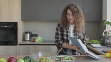 Mutfakta Beklenmedik Tarifler Kitabı 'nı okuyan Şaşırmış Kadın. Doğal Aydınlatma Modern İç Kesimi vurguluyor. Masadaki Taze Malzemeler Davetkar Mutfak Atmosferi Oluştur