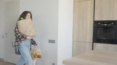Modern mutfağa plastik poşetler ve kağıt torbalarla erzak taşımak. Marketten Dönen Genç Kadın İçin Ev İşleri Konsepti. Eko Yaşam Tarzı, Sağlıklı Yemek, Ev Rutini Ruh Durumu