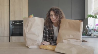 Alışveriş yaptıktan sonra mutfak masasında alışveriş yapan bir kadın. Parlak Modern Mutfak İçi 'nde paketleri boşaltan gevşek kadın. Günlük Rutin Konseptler İçin Mükemmel Sahne