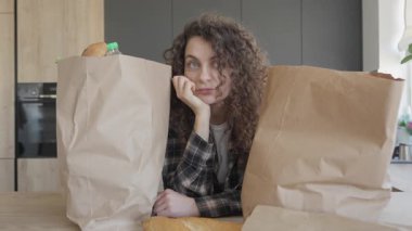 Market alışverişinden sonra dinlenen yorgun bir kadın, mutfak masasında yakın çekim. Günlük yaşamın temaları için mükemmel, ayak işlerinden sonra yorgunluk, doğal ev dekorasyonu, yavaş yaşam, gerçekçi rutinler