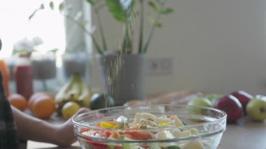 Parlak ev mutfağında taze salata üzerine baharat serpmek. Aromatik Mevsimler Güneş Işığı İçindeki Sağlıklı Yemeği Arttırır. Yemek pişirme, sağlık, ya da sağlıklı yaşam tarzı kavramları için mükemmel klip.