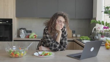 Bright Cozy Kitchen 'da Sağlıklı Yemek sırasında Dizüstü bilgisayar seyreden Odaklanmış Kadın. Modern Yaşam Tarzı Konsantre Kadın Dengeli Beslenme ve Şık Ev İçi Uzaktan Çalışmalar