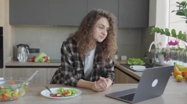 Yakınlarda taze salatayla, rahat mutfakta video dinlerken başını salla. Uzaktan iletişim, ev içi konfor, sağlıklı yaşam tarzı ve çevrimiçi gelişigüzel toplantılar için mükemmel bir görsel temas.