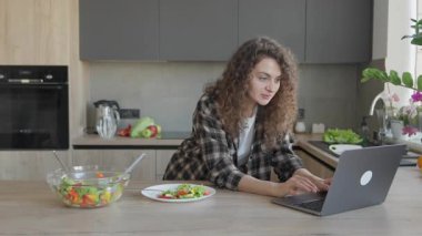 Parlak modern mutfakta konuşurken dizüstü bilgisayarda yazı yazmak. Uzaktan Çalışma Sanal Toplantılar, İç İşleri Rutinleri, Dengeli Sağlıklı Yaşam Stili İçeriği için Mükemmel Sahne. Yüksek kalite 4k görüntü