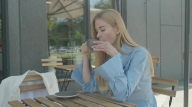 Sarışın kadın açık kafede kahve masasında hayal kuruyor mavi elbiseli. Huzurlu Sabah Sahnesi Düşüncede Kaybolan Genç Kadın, Yavaş Yaşam titreşimlerini kucaklayan, Şık Görünüm