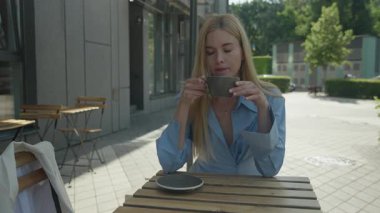 Blonde Woman Enjoying Hot Drink Alone At Outdoor Cafe On Sunny Morning. Peaceful Moment Of Relaxation, Morning Routine, Warm Beverage, Urban Lifestyle, Serene Outdoor Atmosphere