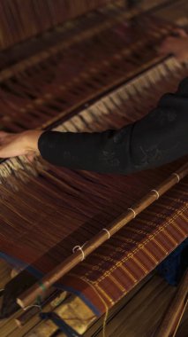 A Baduy woman weaves in front of her home using traditional tools. Her skilled hands create beautiful patterns, preserving cultural heritage and artistry. clipart