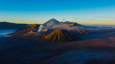 Bromo Dağı 'nda çarpıcı bir gündoğumu canlı bir günbatımını gözler önüne seriyor. Bulutlar zirveyi zarifçe kaplıyor ve Doğu Java' nın doğal güzelliğini gözler önüne seriyor..