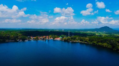 Ranu Bedali Lake in East Java sparkles under a clear blue sky, with Mount Semeru majestically rising in the background. The stunning clouds add to the serene beauty of this breathtaking landscape. clipart